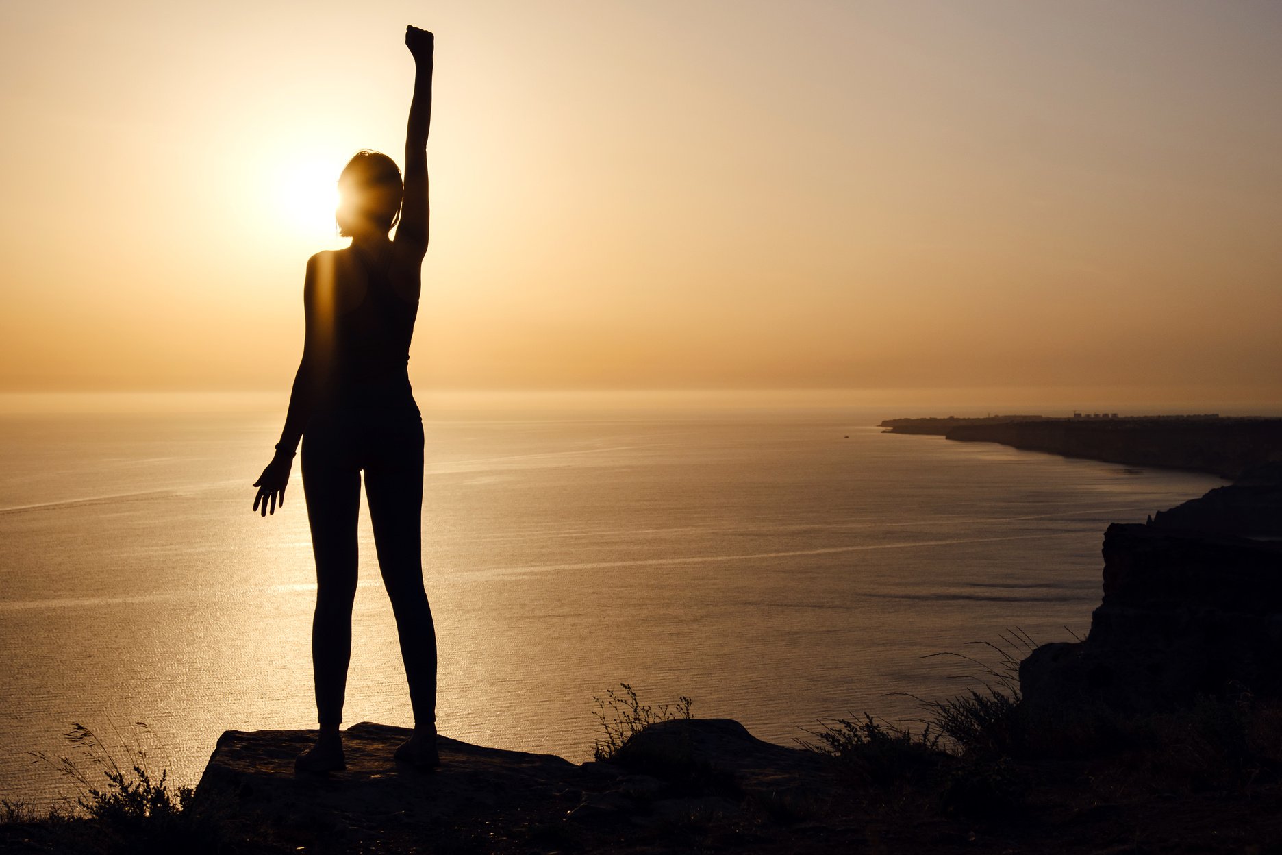 silhouette of woman with raised hands on the beach at sunset